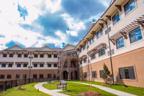 Exterior view of a senior living facility with a courtyard, benches, and a walkway.