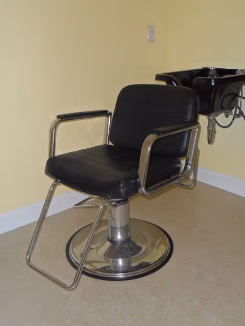 Black salon chair with chrome frame beside a hair washing sink in a care home.