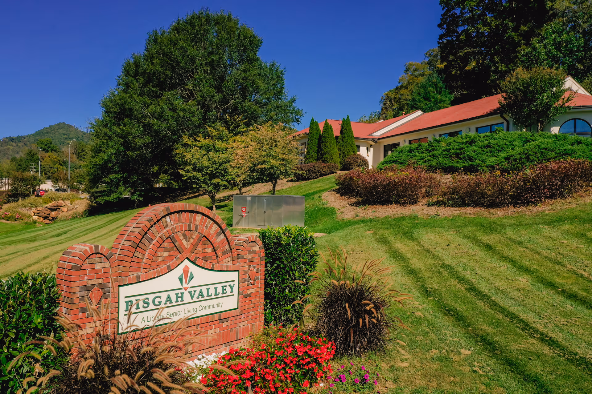 Brick entrance sign reading "Pisgah Valley" in front of a landscaped lawn and a single-story retirement community building.