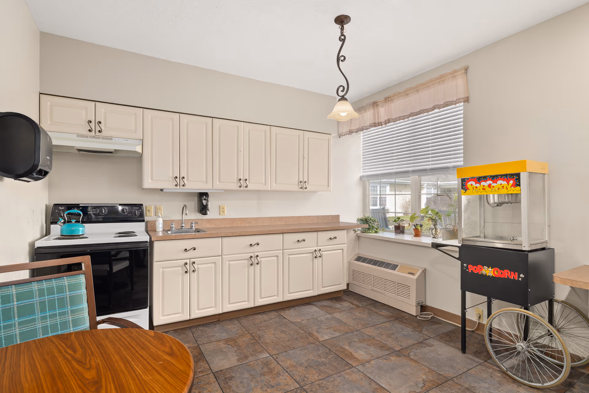 Bright kitchen with white cabinets, a stove and sink, a popcorn machine by the window and a small round dining table.