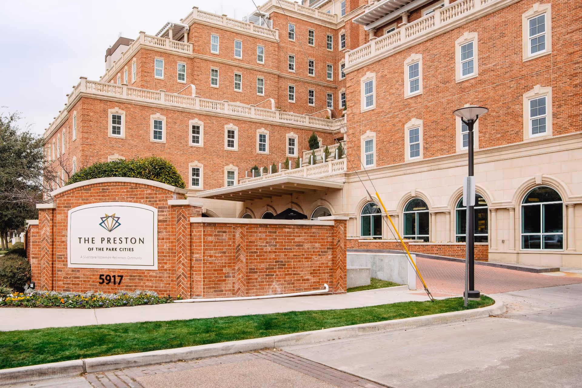 Front entrance and sign for The Preston of the Park Cities, a multi-story brick building.