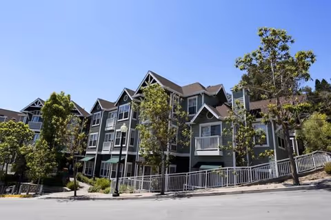 Exterior view of a multi-story senior living building with balconies and surrounding trees.