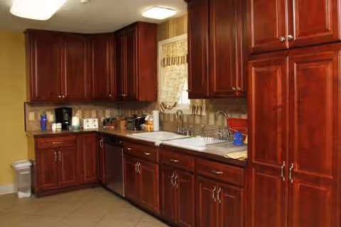 U-shaped kitchen with dark wood cabinets, white sink, and stainless appliances along granite counters.