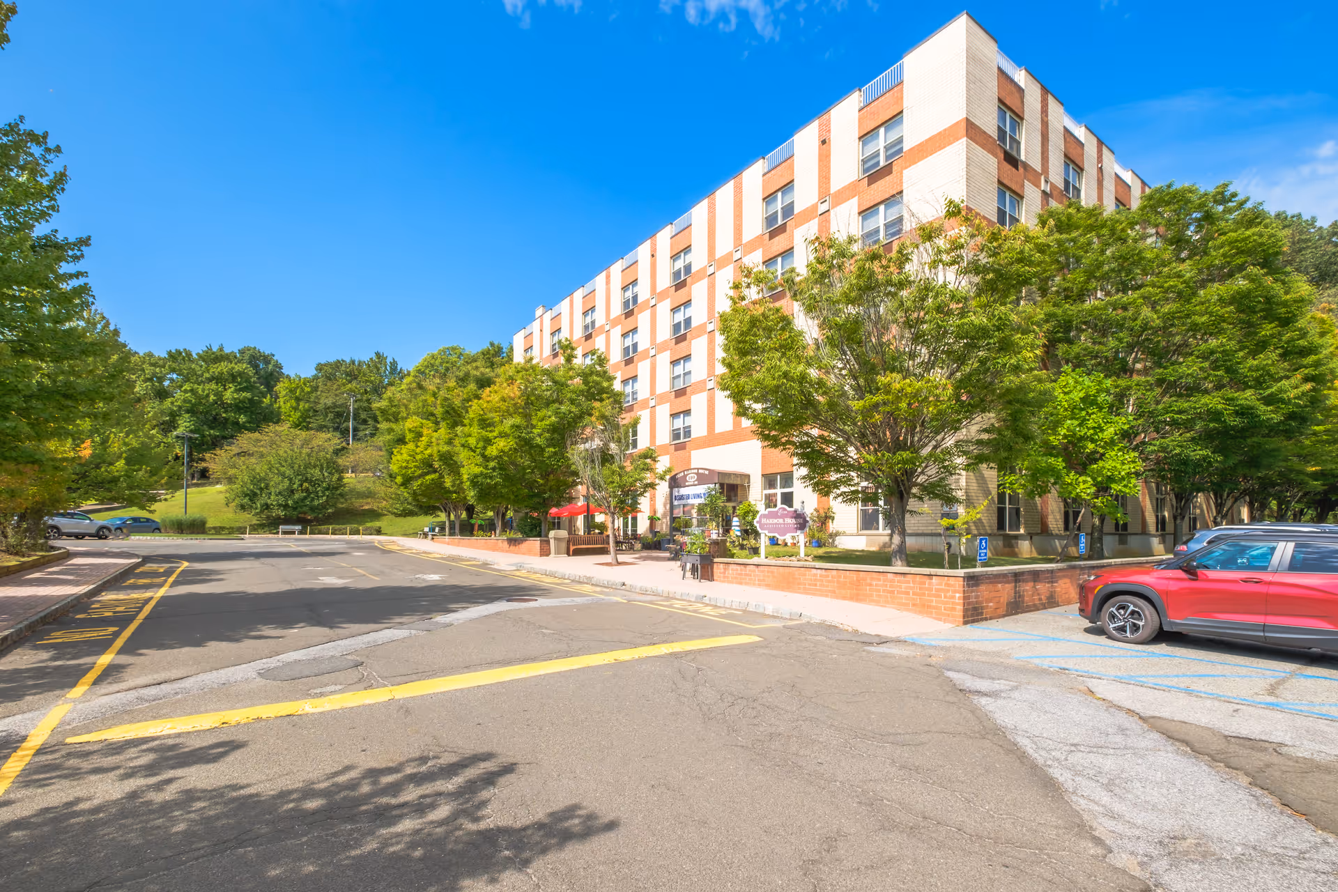 Exterior view of a multi-story senior living facility named Eger Harbor House with a parking area, trees, and a clear blue sky.