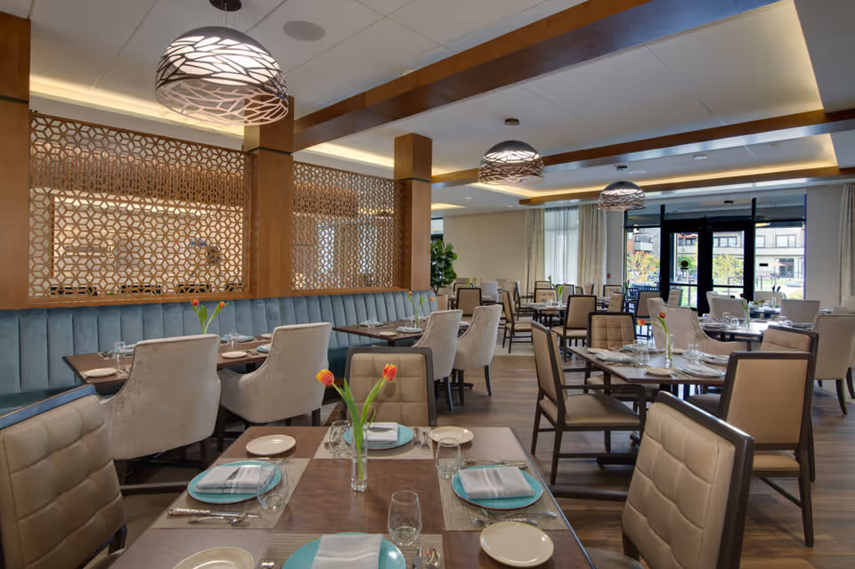 Well-appointed dining room with multiple set tables, upholstered chairs, pendant lights, and a decorative wood partition.