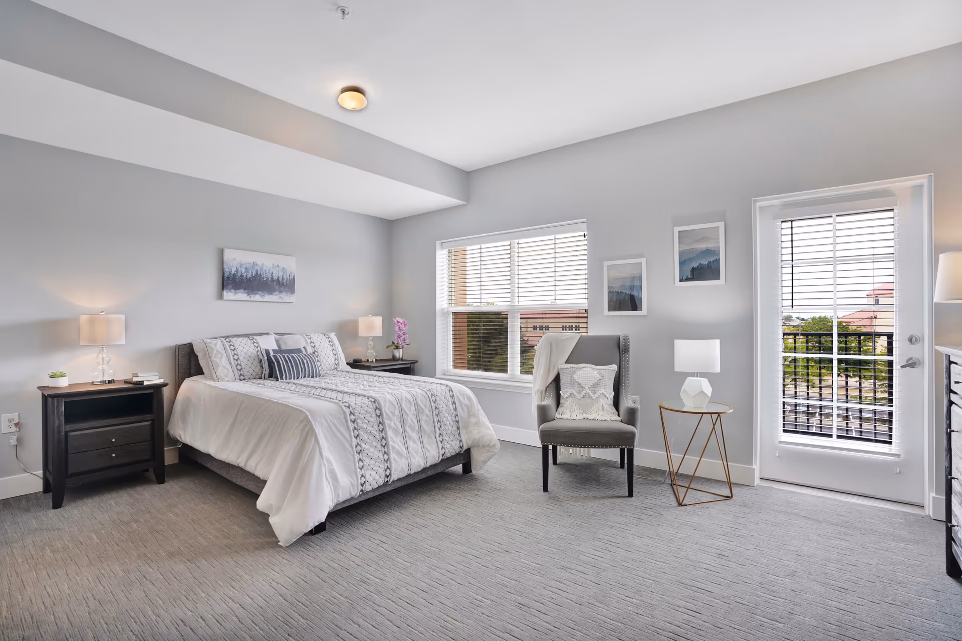 Bright, modern bedroom with a made bed, two nightstands, an armchair, and a glass door leading to a small balcony.
