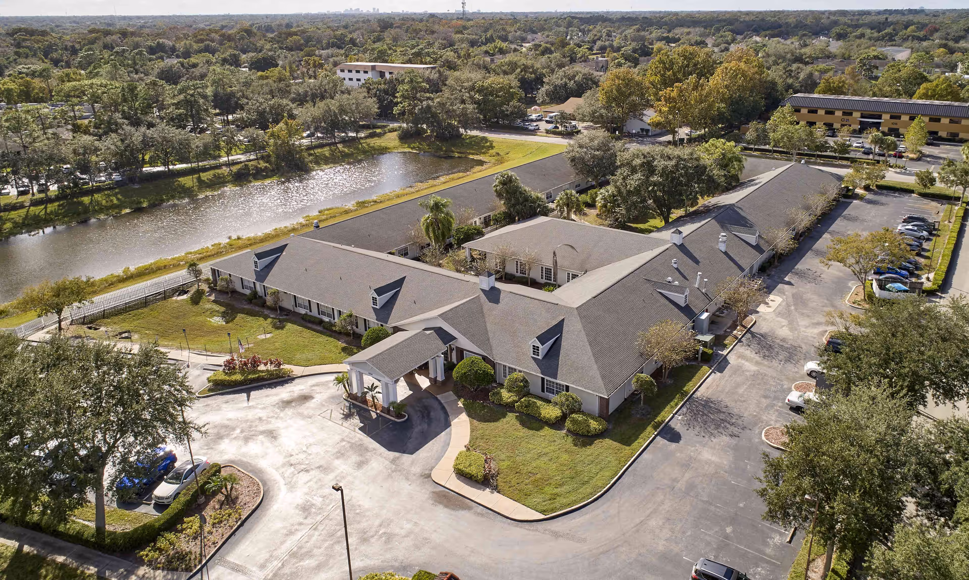 Aerial view of Palmetto Landing senior living facility showing a large single-story building with a covered entrance, surrounded by trees, parking lots, and a nearby pond with a walking path.
