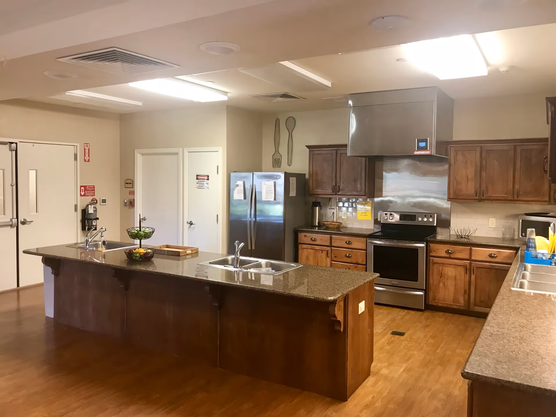 Communal kitchen with a large island, dual sinks, stainless steel appliances and wooden cabinets.
