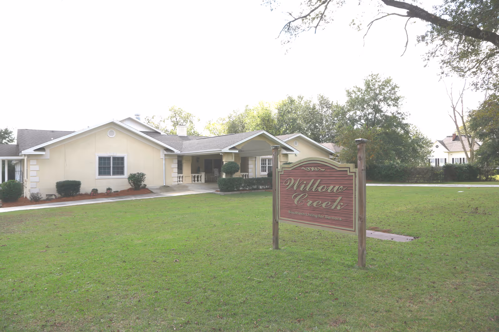 Single-story building and front lawn with a wooden sign reading "Willow Creek" marking the senior living facility.