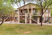 Two-story beige senior living building with stairs and trees in front.