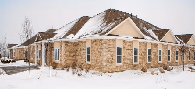 Snow-covered single-story stone-clad building with multiple gabled roofs and surrounding snowy grounds.
