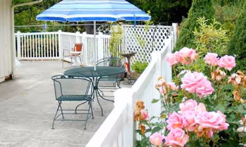 Outdoor patio with metal table, chairs, blue umbrella, and pink roses along white railing.