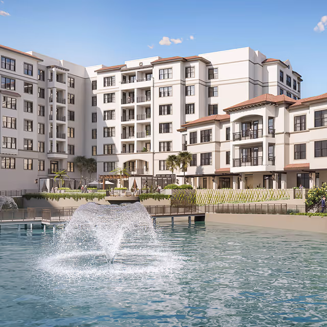 View of a multi-story senior living facility named The Waterford with a large water fountain in a pond or pool in the foreground, surrounded by landscaped greenery and outdoor seating areas under a clear blue sky.