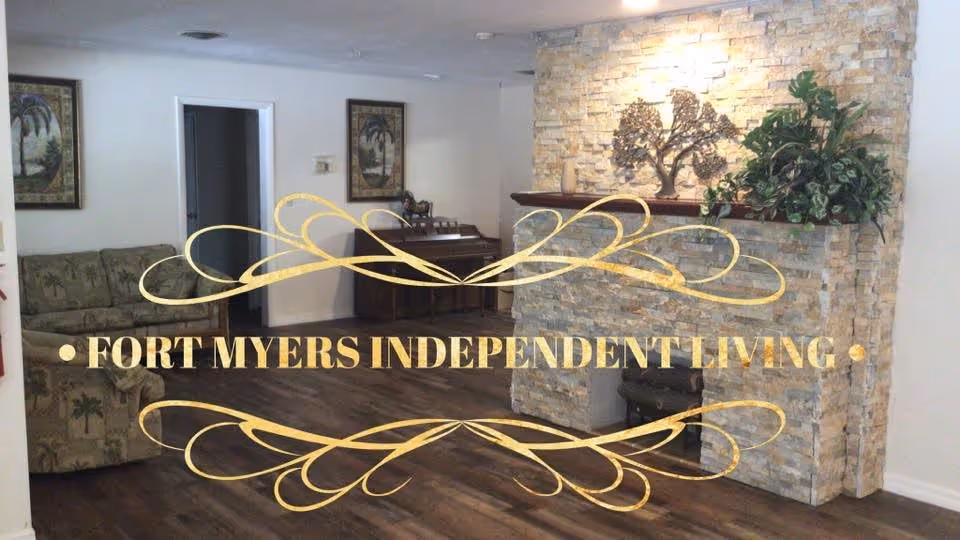 Interior view of a living room area with wooden flooring, a stone fireplace decorated with a metal tree sculpture and plants, a patterned sofa, two framed pictures on the wall, and a wooden cabinet. The image has a decorative gold text overlay that reads 'FORT MYERS INDEPENDENT LIVING'.