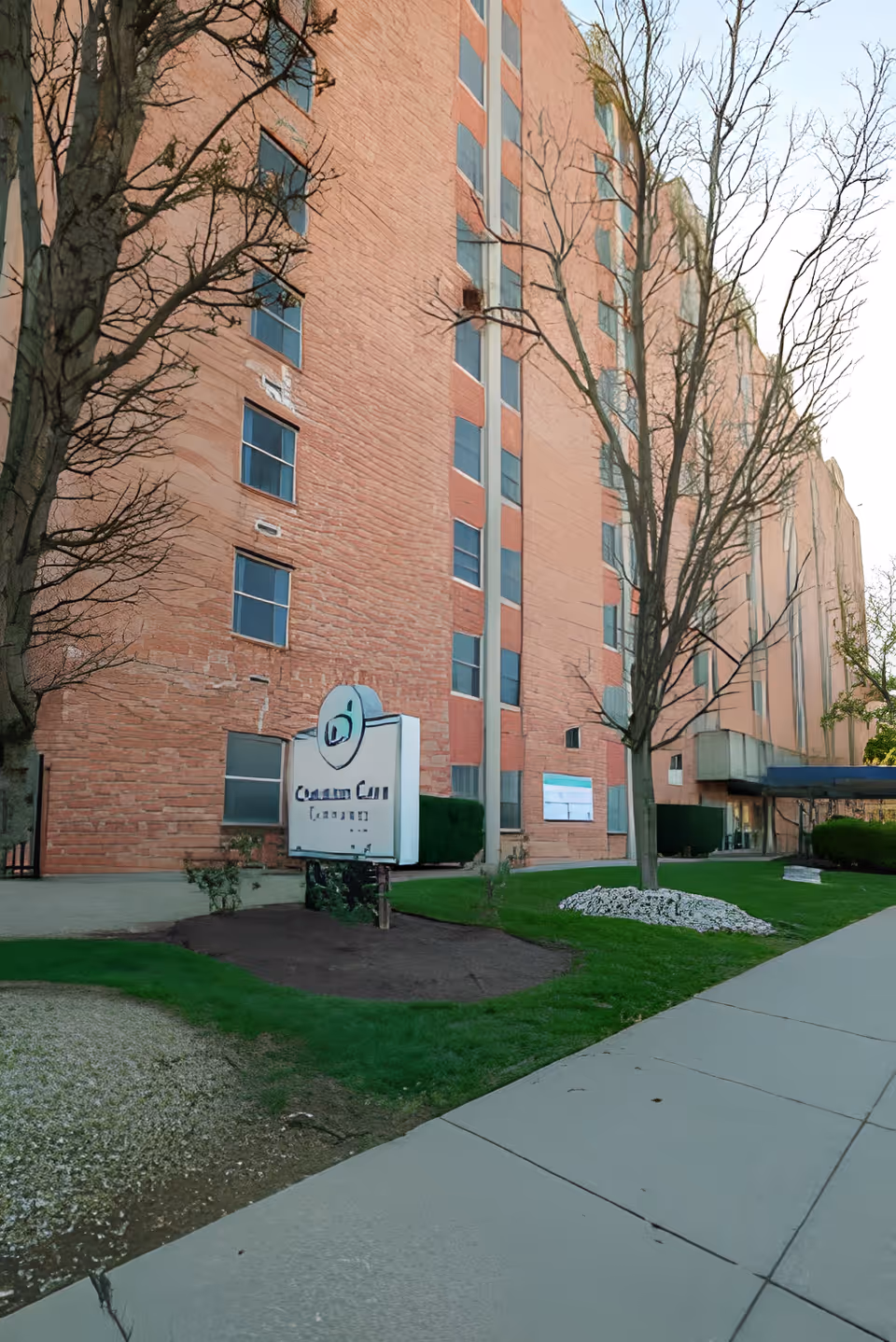Exterior view of a multi-story brick building with several windows and a sign in front that reads 'Covenant Care Louisville'. There are leafless trees and a well-maintained lawn with a sidewalk leading to the entrance.