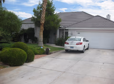 Front exterior of a single-story house with a driveway, a parked white car, garage, and landscaped yard.
