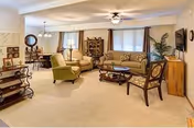Spacious furnished living room with sofas, chairs, a coffee table, and a dining area visible in the background.