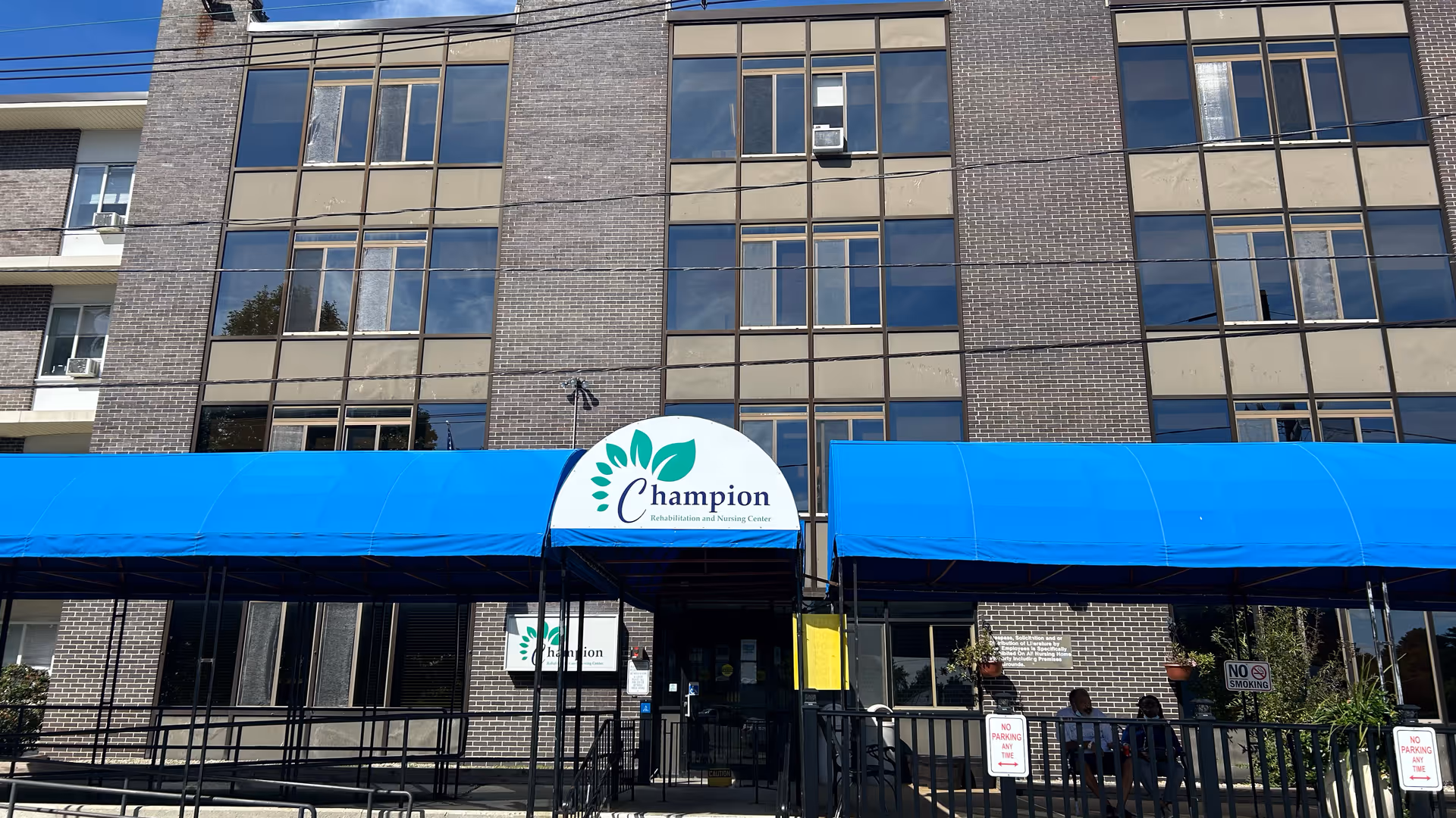 Front exterior of a multi-story brick building with blue awnings and a 'Champion' sign above the entrance.