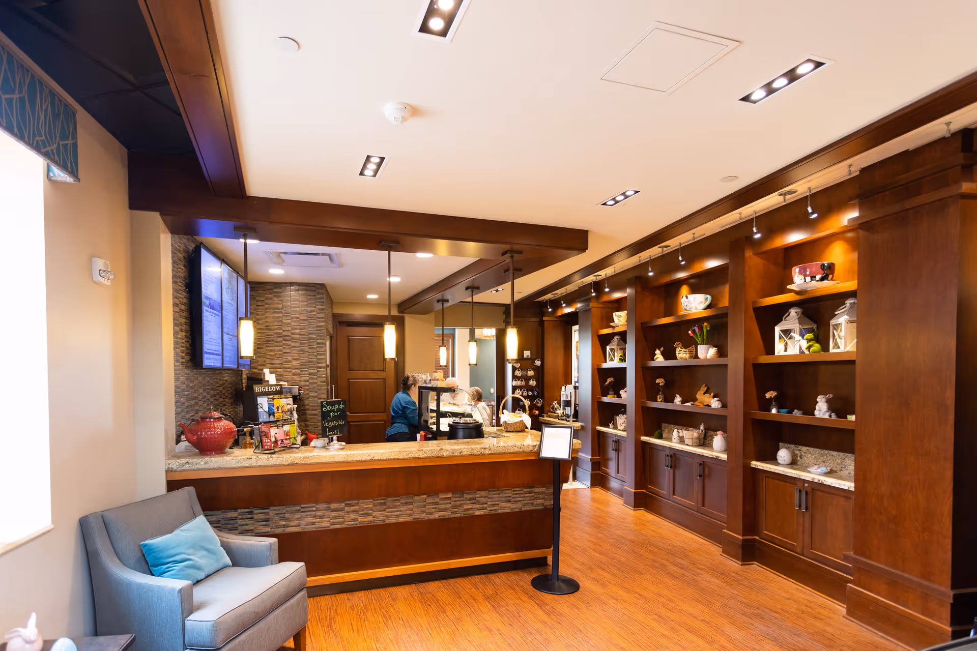 Lobby reception area with a front desk, staff behind the counter, seating, and wood shelving displays.