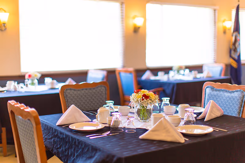 Dining room tables set with plates, folded napkins, glassware and a floral centerpiece.
