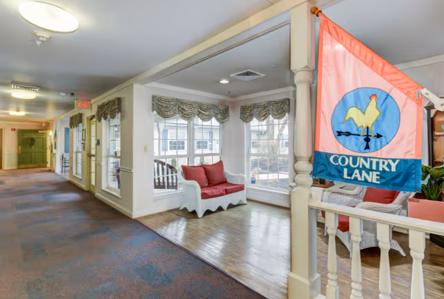 Bright interior hallway seating area with wicker benches and red cushions by bay windows and a 'Country Lane' flag.