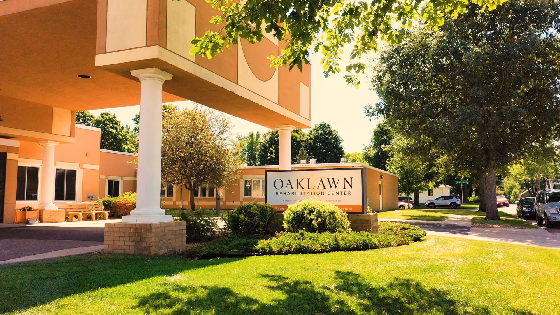 Front entrance and sign for Oaklawn Rehabilitation Center with columns, landscaped lawn, and trees.