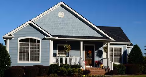 Blue-gray single-story house with front porch and manicured shrubs.