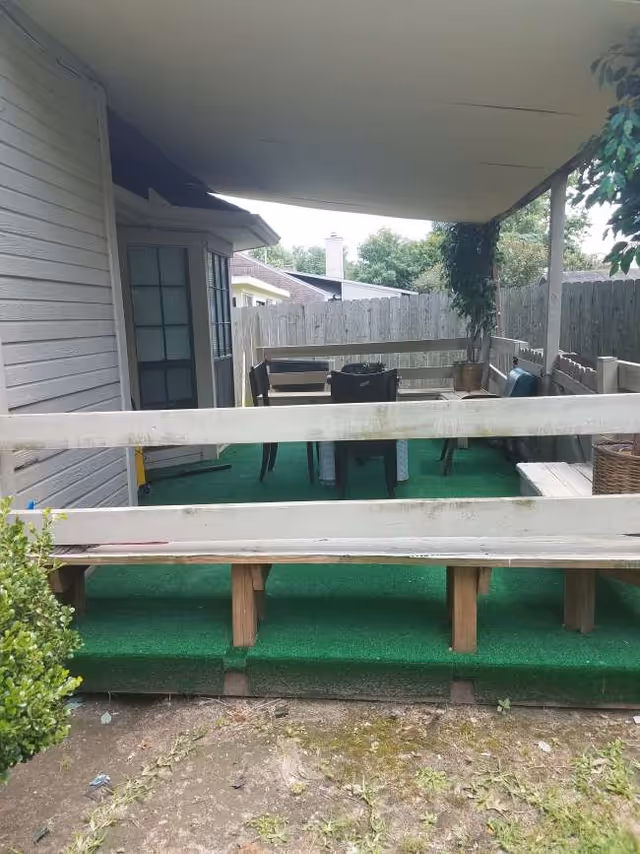 Covered outdoor patio with green turf, railing, and dining furniture.