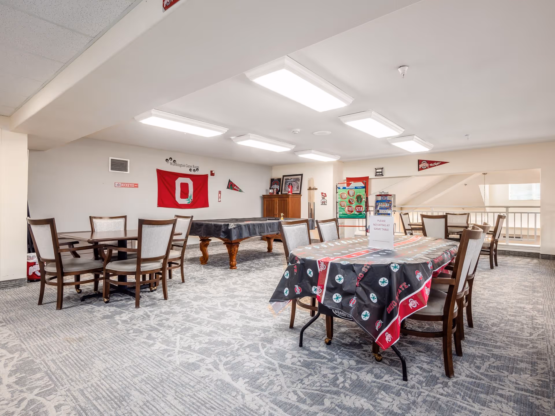 Bright interior community room with multiple tables and chairs, a covered pool table, and Ohio State-themed decorations on the walls and tables.
