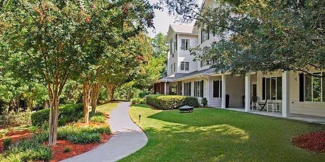 Curved walkway through a landscaped lawn beside a multi-story white building with trees and a covered porch.