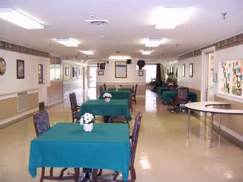 Senior living dining area with teal tablecloths, flowers, and cushioned chairs along a corridor.