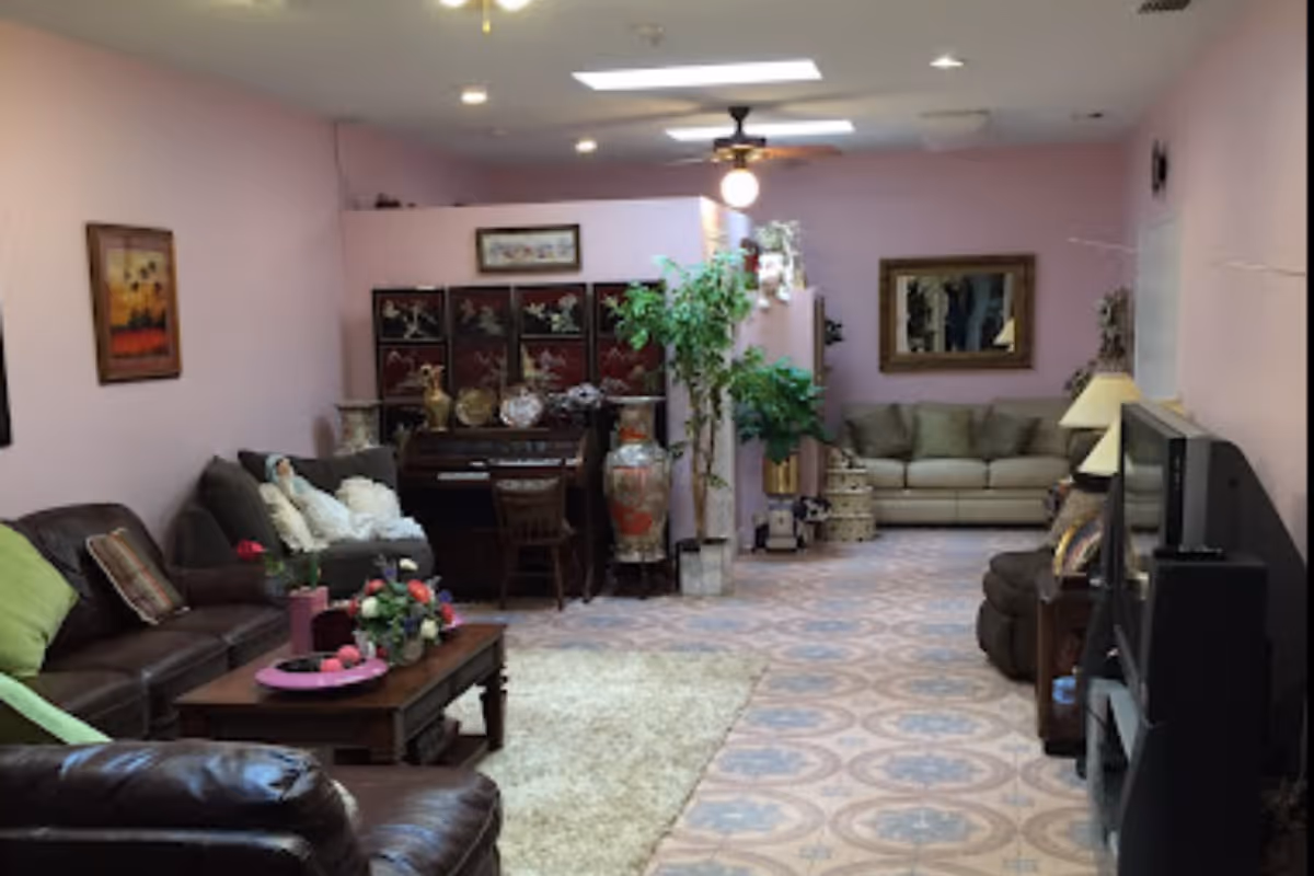Communal living room with sofas, a coffee table, TV, piano, plants, and pink walls.