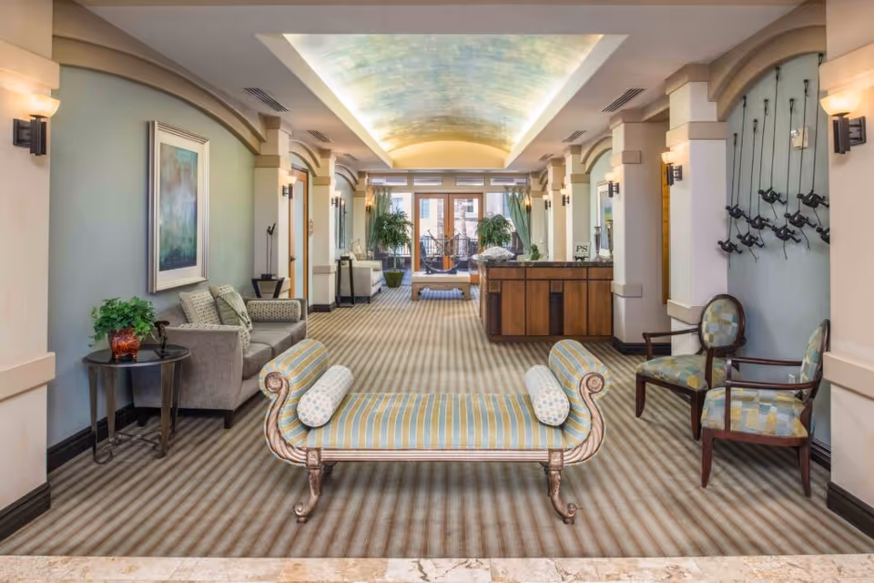 Spacious elegant lobby with a striped bench in the foreground, upholstered chairs, a reception desk and decorative arched ceiling.