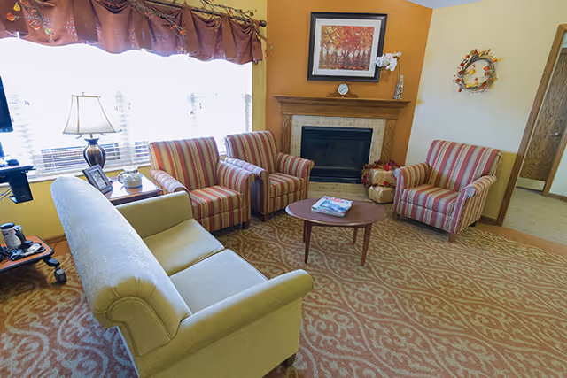 A cozy communal living room with a sofa, three striped armchairs around a coffee table and a fireplace.