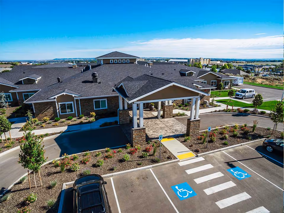 Exterior front view of a single-story memory care building with a covered porte-cochère, landscaped grounds, and marked accessible parking spaces.