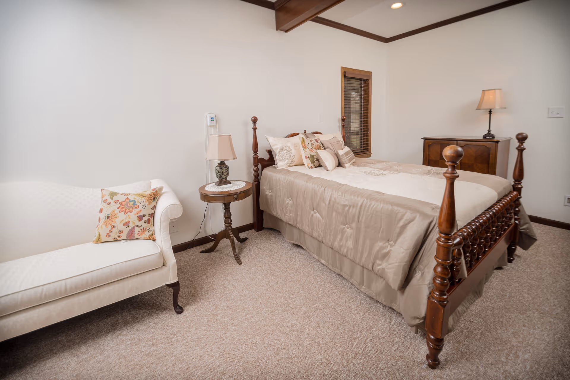 A cozy bedroom featuring a wooden four-poster bed, an upholstered chaise lounge, side tables and lamps.
