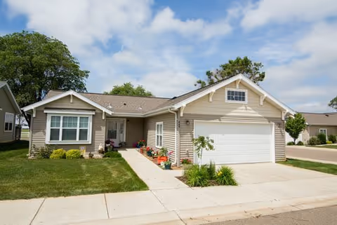 A single-story senior living facility exterior with a two-car garage, front walkway, and manicured lawn.
