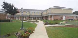 Exterior view of Oak Wood Place Assisted Living showing a brick walkway and manicured lawn.