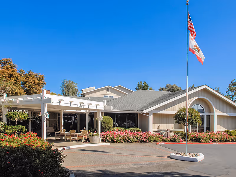 Front exterior view of Holiday Springs of Napa with entrance, patio seating, and flagpole.