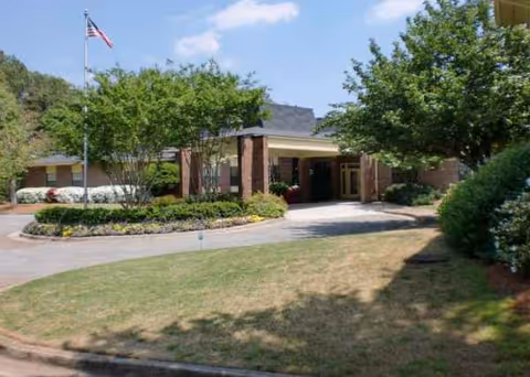 Senior living facility front entrance with brick facade, flagpole, and landscaped circular driveway.