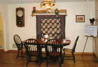 Round wooden dining table with six chairs in a room featuring a wall quilt.