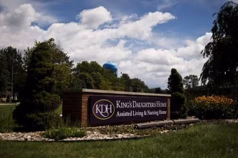 Outdoor view of the Kings Daughters Home sign with landscaped front yard and trees in distance.