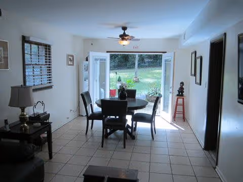 Dining area with a round table and four chairs facing open French doors that lead to a grassy backyard.