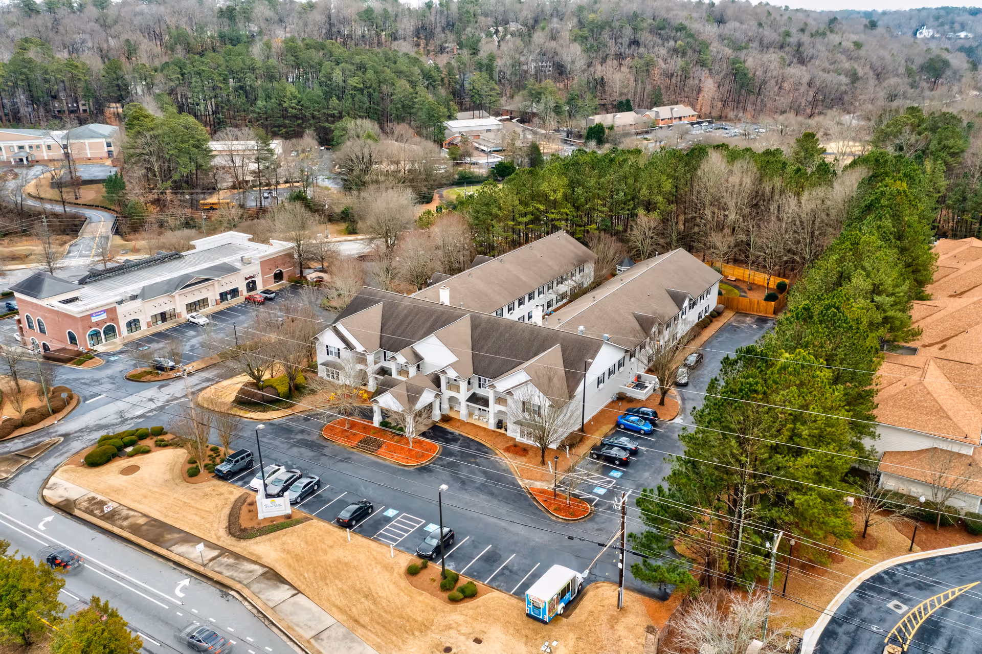 Aerial view of TerraBella Roswell facility showing a large two-story building with a parking lot in front, surrounded by trees and other buildings. The area includes paved roads, landscaped grounds, and a wooded backdrop.