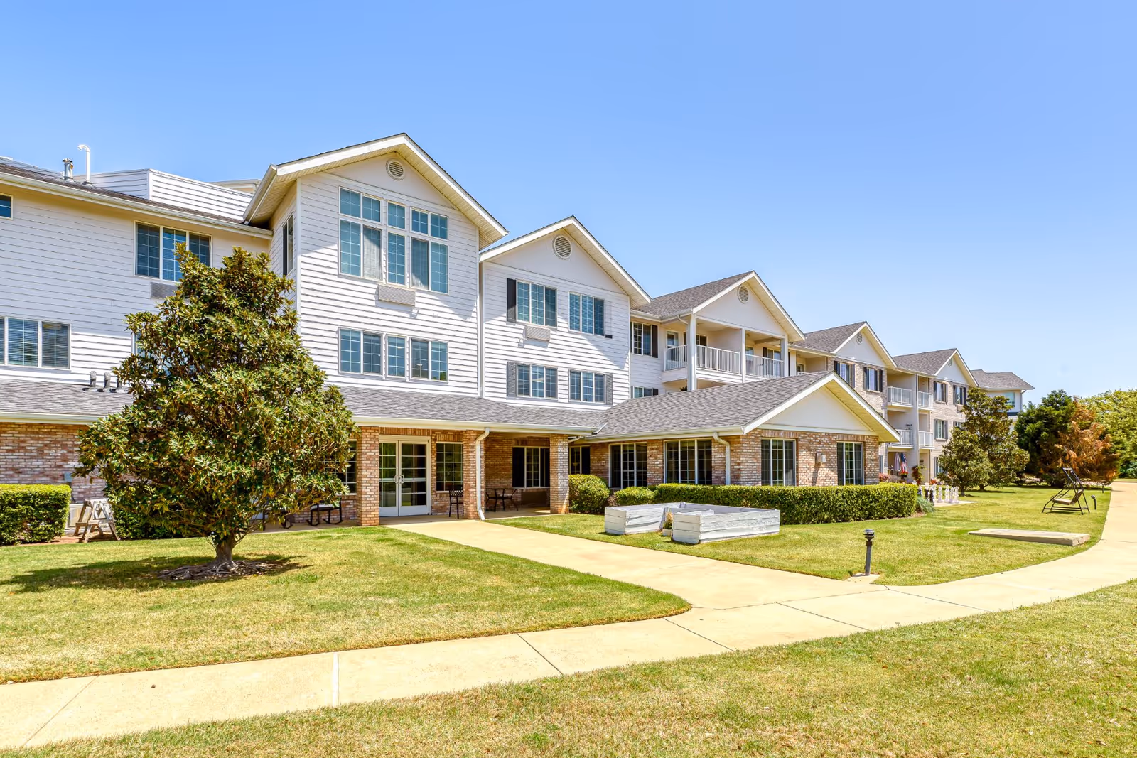 Sunny exterior view of a multi-story senior living building with landscaped lawn.