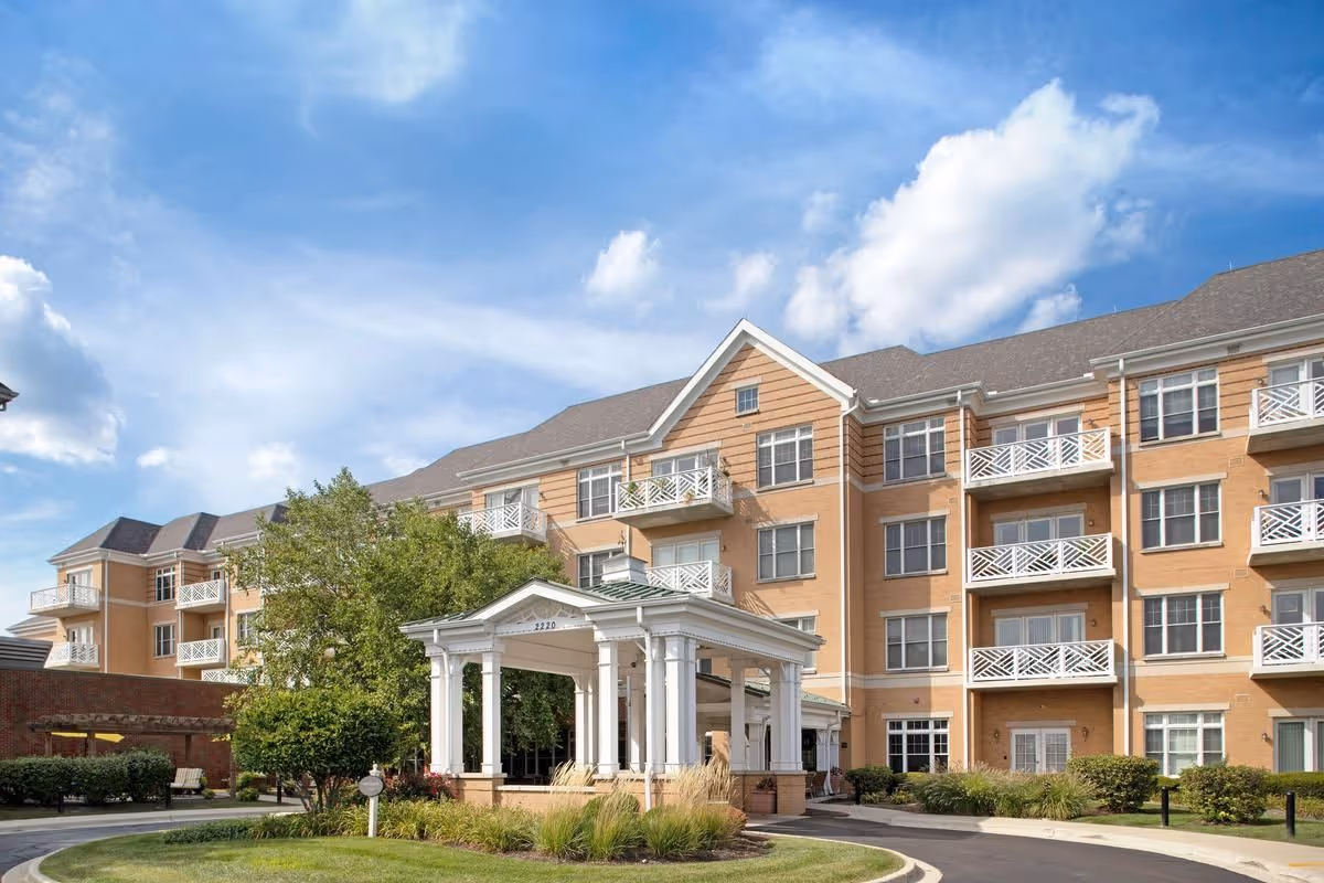 Exterior front entrance of a multi-story senior living building with a covered porte-cochère and balconies.