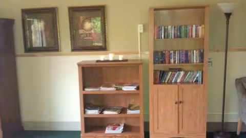 Interior common area with a wooden bookshelf, cabinet, framed art, floor lamp, and seating.