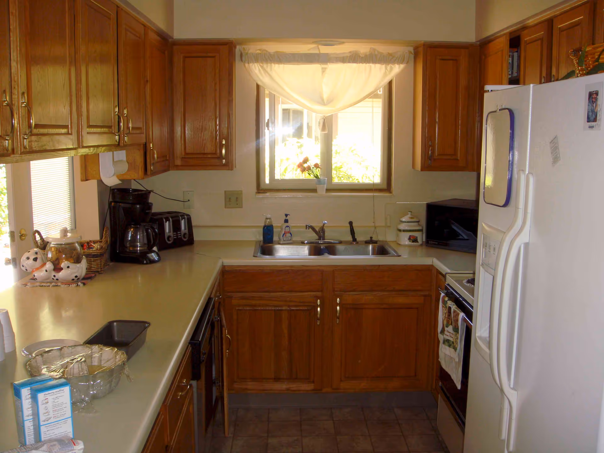 Kitchen with oak cabinets, a double sink under a curtained window, countertops with appliances, and a white refrigerator.