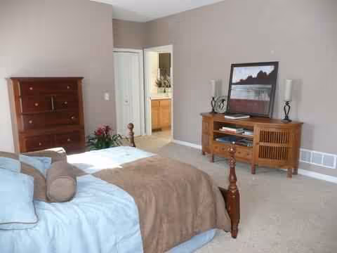 A cozy adult bedroom in a senior facility with a bed, dresser, and TV stand.