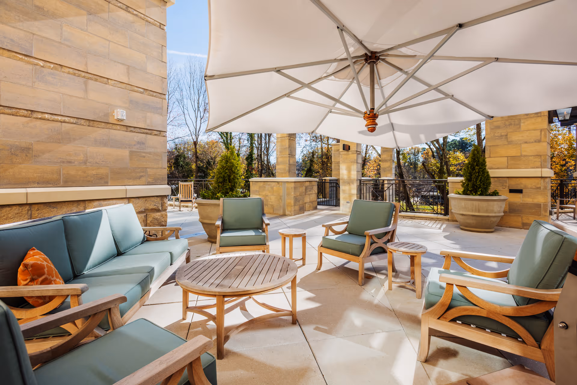 Outdoor patio seating area with cushioned wooden chairs, round tables, and a large umbrella.